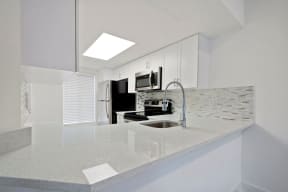 Kitchen with long counter top, tiled back-splash and stainless steel refrigerator, microwave, and oven