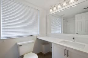 Bathroom with window above toilet, vanity, sink, cabinets, mirror, and lighting