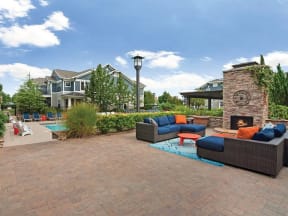 outdoor living room with gas fire place on a stone patio located next to pool area and lush landscaping