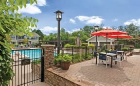 outdoor stone patio seating area with umbrella-covered dining tables next to fenced pool area