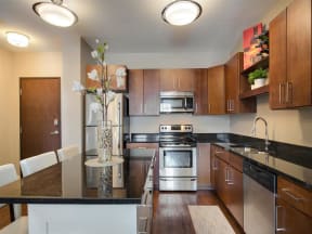 Be @ Axon Green  Apartment Kitchen with Wood Cabinets, Black Granite Island, and Stainless-Steel Appliances