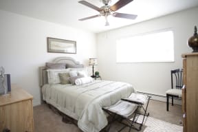 Bedroom with dark ceiling fan, bed has light bedding with window on the left wall.