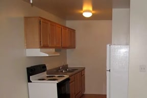 Galley style kitchen with cherry color cabinets, a white electric stove, and white fridge.
