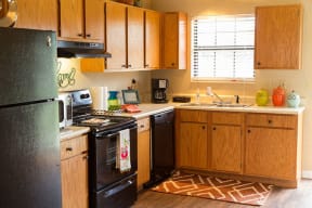 City Edge Flats Equipped Kitchen with Black Appliances, Wood-Style Flooring, and Ample Cabinet Storage