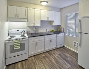 Kitchen with white cabinets and grey countertops. Image contains a white oven, sink and white dishwasher. One window and wood style flooring.