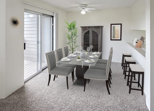 Dining area with table and chairs in the center, a ceiling fan with light, sliding glass doors to the left and a breakfast bar on the right.