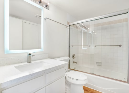 Apartment bathroom with vanity, illuminated mirror, toilet, and shower tub combo.