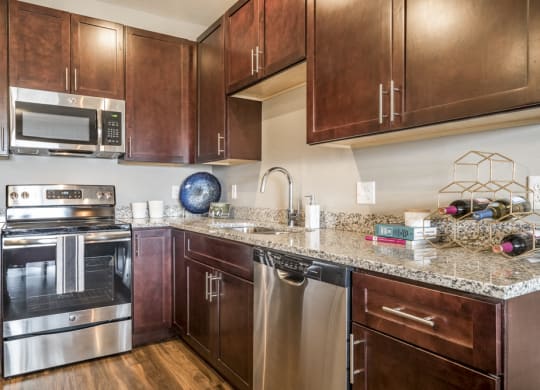 Kitchen featuring light granite countertops, dark cabinetry and stainless-steel appliances at 360 at Jordan West best new apartments West Des Moines IA 50266