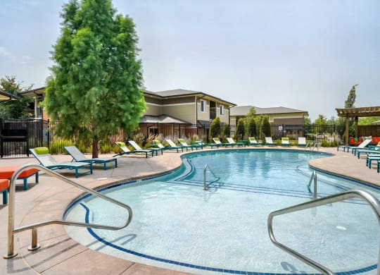 Organically shaped resort style pool surrounded a pool deck with bright blue lounge chairs