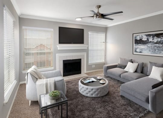 Model living room carpet and 3 large windows with TV above fireplace in middle.