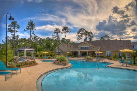 Resort-style swimming pool with lounge chairs with view of the resident clubhouse at Lullwater at Blair Stone apartments for rent in Tallahassee, FL