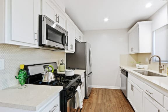 Renovated kitchen with stainless steel French door refrigerator, gas stove over microwave range hood, dishwasher, single kitchen sink, wood style floors, white cabinets, light quartz counter tops, tile backsplash