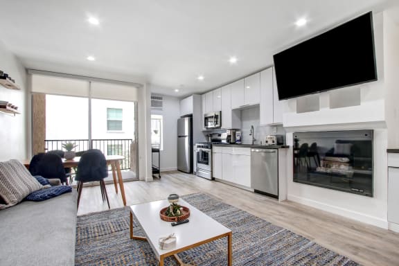 Furnished 1 Bedroom Suite, living room with cozy fireplace, dining area on the left with private balcony, open kitchen