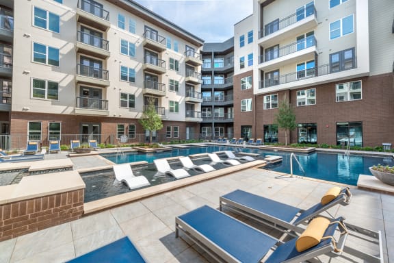 Pool courtyard with pool in the middle and chairs around pool with view of apartment building and balconies and tanning chairs