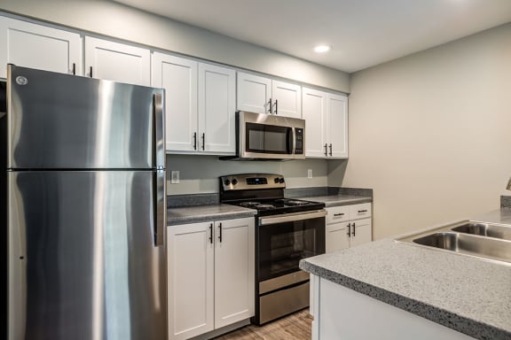 Apartments for Rent in Fife- Bella Sonoma Kitchen with Stainless Appliances, Grey Countertops, White Cabinetry, and Wood-Style Flooring