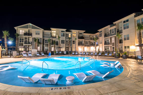 an outdoor pool with lounge chairs at night