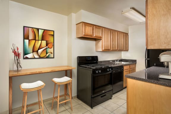 kitchen at Grandview apartments in Falls Church, VA with black appliances, light wood cabinets and tile flooring and long wood kitchen table with two stools