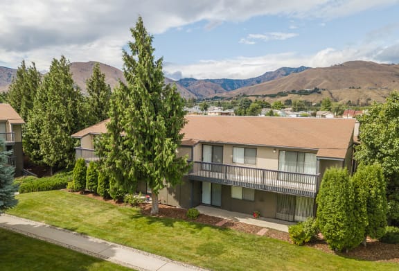 Exterior of apartments with green grass, trees and mountain range in the background.