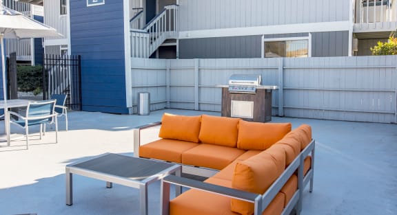 Outdoor resident lounge with organge patio couch, a coffee table, umbrella covered seating and a BBQ.