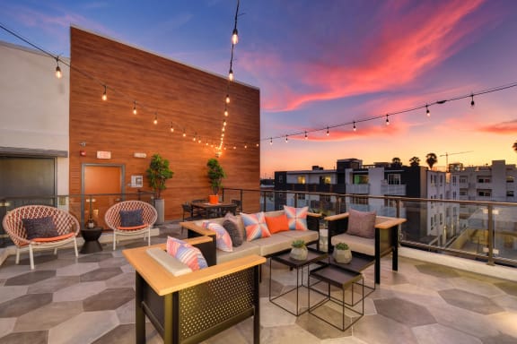 Community rooftop lounge area at dusk with colorful sunset.  Lounge area has table chairs and couches.
