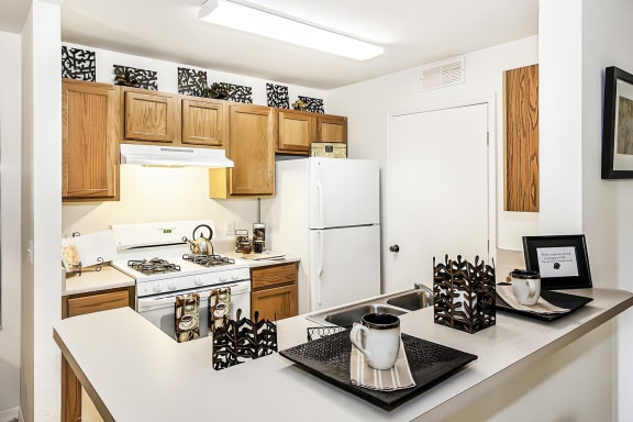 Model apartment kitchen with white appliances, brown cabinets, and breakfast bar.
