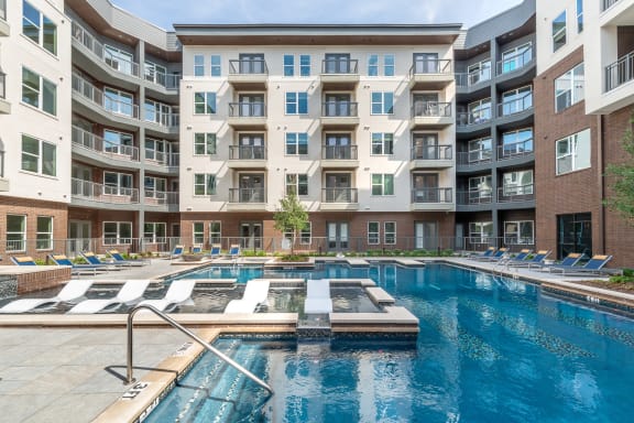 Pool courtyard with pool in the middle and chairs around pool with view of apartment building and balconies