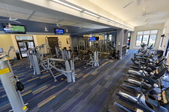a large fitness room with cardio equipment and flat screen tvs