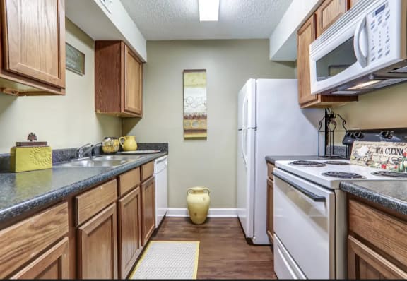 Medium brown wood flooring and cabinetry with beige walls and white appliances.