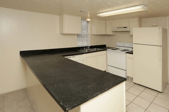 Fully equipped white kitchen wiht black countertops and white tile floor.
