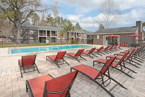 Expansive sundeck and pool. Red lounge chairs are lined up on the sundeck.