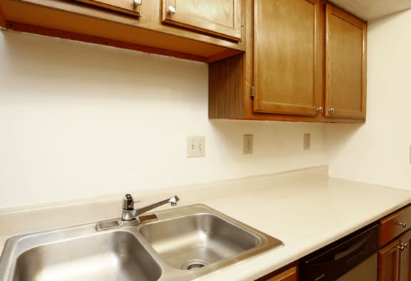 Medium brown cabinetry with beige counter and double stainless sink.