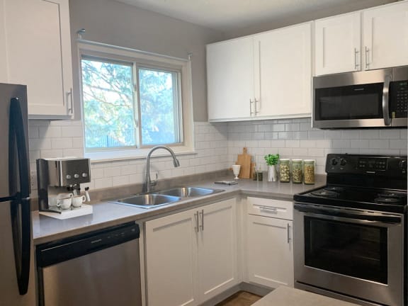 Apartment with updated kitchen finishes featuring subway tile backspash, stainless steel appliances, plan wood flooring, and new white cabinetry