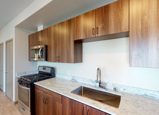 Modern kitchen with stainless steel appliances,  brown cabinetry, and quartz countertops at Brownstone Apartments in Las Vegas, Nevada