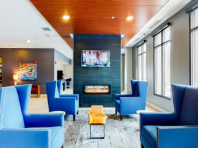 Lobby area with blue lounge chairs, floor to ceiling fireplace with mounted TV above