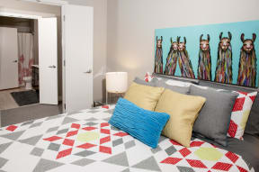 Master bedroom leading into walk through closet and private bathroom. Bed is staged with a brightly colored comforter and a large piece of art hangs above the headboard.