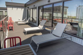 Rooftop patio furnished with lounge chairs and three tables for seated work or dining.
