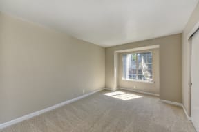 Bedroom with pop- out style window.  Lots of natural sunlight.  Beige walls and light colored carpeting. 