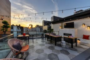 Community rooftop lounge area at dusk.  Area is equipped with chairs, couches, flat screen TV mounted on the wall and views of the city 
