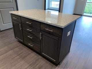 Dark brown kitchen island with light granite counters and storage doors along the front