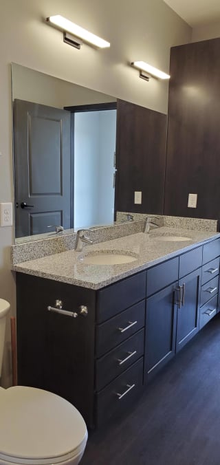 Dark brown bathroom vanity with light granite and dual vanities and linen closest