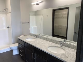 Bathroom with walk in shower, dark brown cabinets and  two sinks in two bedroom apartment at Haven at Uptown