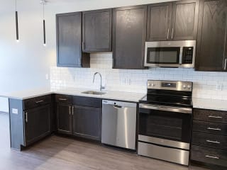 Nest Studio Floor Plan in Mocha Finish at Haven at Uptown Kitchen with warm brown upper and lower cabinets, white subway tile, and stainless steel appliances