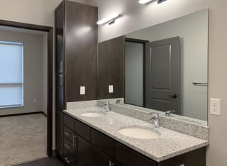 bathroom with dual sinks and dark brown cabinets and storage closet