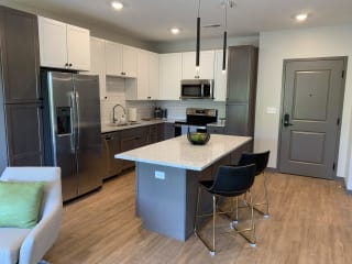Furnished kitchen in the Slate finish with two tone cabinets, hard wood style flooring, and granite counter tops in the Bliss floor plan at Haven at Uptown