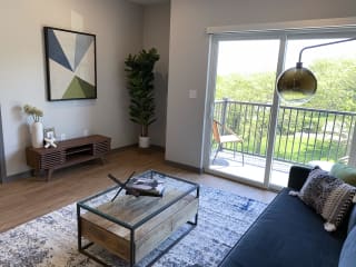 Spacious furnished living room with hard wood style flooring and scenic view of tree line in Lincoln at Haven at Uptown.