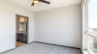 Shine (2 bed, 2 bath) in Slate finish Master bedroom with large windows providing natural light, ceiling fan, and attached bathroom at Haven at Uptown in Lincoln, NE