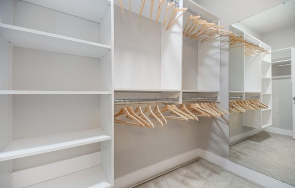 a walk in closet with white shelves and wooden hangers