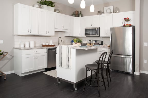 Contemporary kitchen with white cabinetry, pendant lighting, and stainless steel appliances. Kitchen island is the focal point of the kitchen area with seating for entertaining.