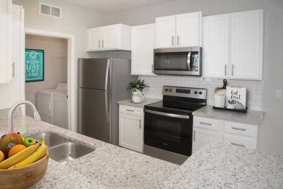 Full kitchen with white cabinets, stainless steel appliances and wrap around granite countertop