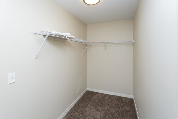 Large, empty closet with white walls, overhead lighting and shelf near ceiling